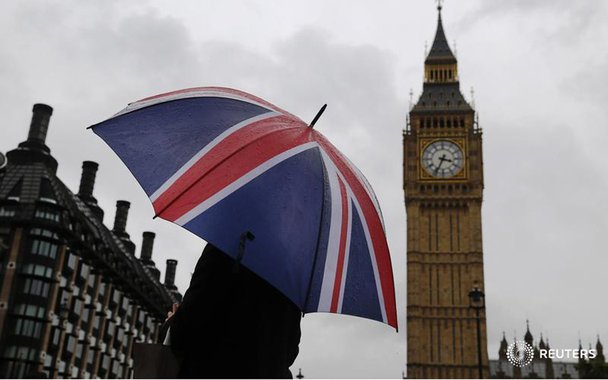 A woman holds a Union flag umbrella in front of the Big Ben clock tower (R) and the Houses of Parliament in London October 4, 2014. REUTERS/Luke MacGregor (BRITAIN - Tags: ENVIRONMENT CITYSCAPE TRAVEL) - RTR48XA7