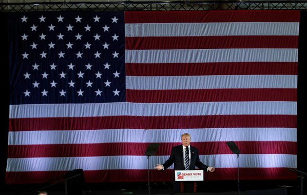 U.S. President-elect Donald Trump speaks beneath a giant American Flag during a "Thank You USA" tour rally in Baton Rouge, Louisiana, U.S., December 9, 2016. REUTERS/Mike Segar