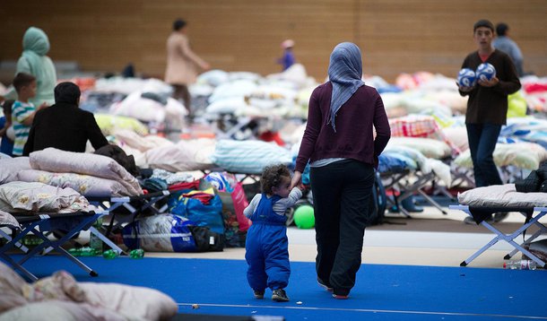 In this Saturday Sept. 12, 2015 picture refugees and migrants walk in a sports hall in Berlin that was turned into a asylum-seeker accommodation . ( Kay Nietfeld/dpa via AP)