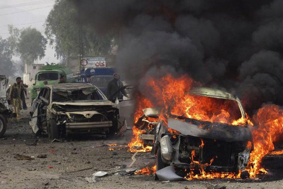 A police officer and a citizen walk towards a burning car after a bomb attack, at Fauji Market in Peshawar December 17, 2012. At least 12 people were killed on Monday when the blast struck the market area in Pakistan's volatile tribal belt, a security off