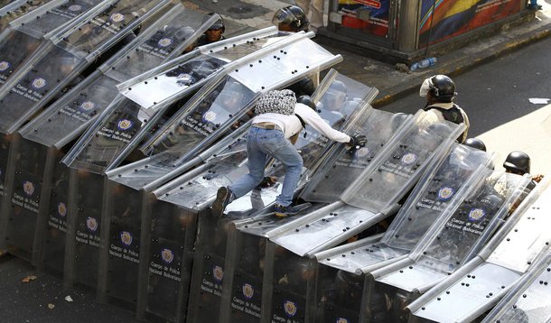 A demonstrator jumps on shield wall formed by riot police during a protest against Venezuela's President Nicolas Maduro's government in Caracas February 12, 2014. One person (not pictured) was killed during standoffs at the end of the anti-government rall