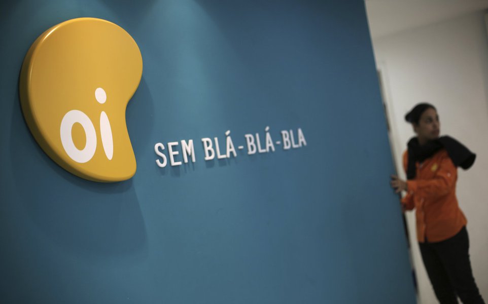 A woman stands next to the logo of Brazil's largest fixed-line telecoms group Oi, inside a shop in Sao Paulo October 2, 2013. The planned combination of Brazil's Oi SA and Portugal Telecom SGPS SA is unlikely to face opposition from Brazil's antitrust reg