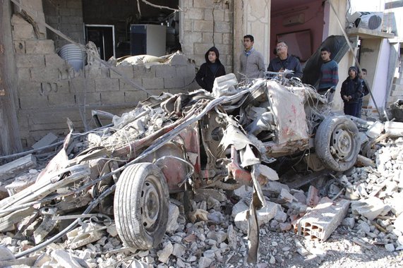 People gather around the wreckage of a car bomb in the village of Al-Kafat, in central Hama province January 9, 2014, in this handout photograph released by Syria's national news agency SANA. At least 18 people, including women and children, were killed b