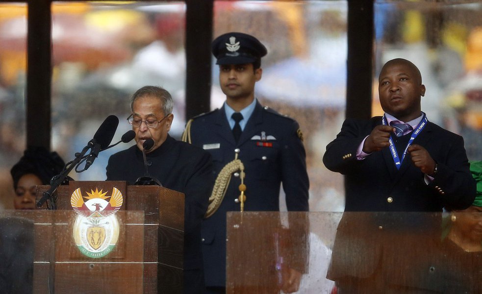 India's President Pranab Mukherjee speaks at the podium as a sign language interpreter (R) punches the air beside him during a memorial service for late South African President Nelson Mandela at the FNB soccer stadium in Johannesburg December 10, 2013. Th