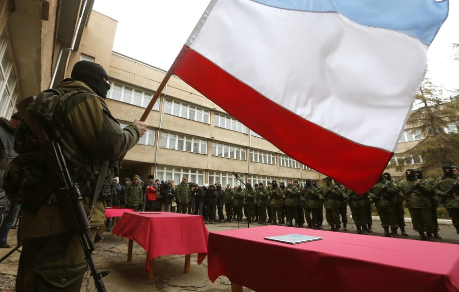 An armed man, believed to be a Russian serviceman, holds a Crimea flag as members of a pro-Russian self defence unit stand in a formation before taking an oath to Crimea government in Simferopol March 10, 2014. Russian forces consolidated their hold on Uk