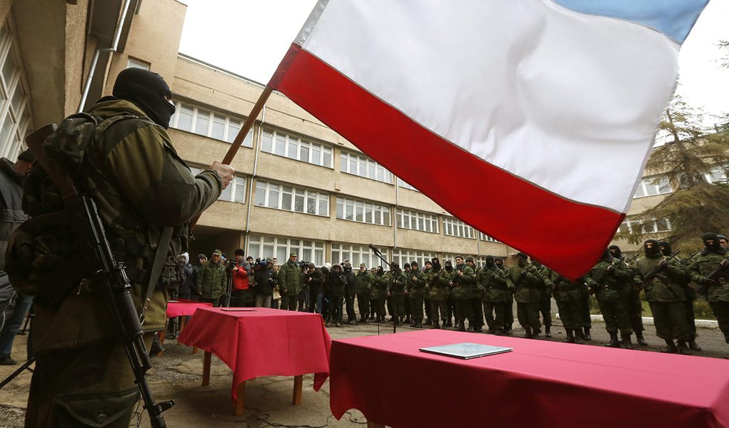 An armed man, believed to be a Russian serviceman, holds a Crimea flag as members of a pro-Russian self defence unit stand in a formation before taking an oath to Crimea government in Simferopol March 10, 2014. Russian forces consolidated their hold on Uk
