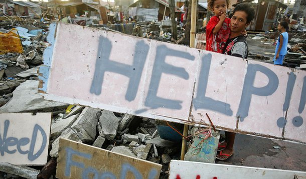 Survivors stand by messages asking for help for their community in an area totally devastated by Typhoon Haiyan in Tacloban November 21, 2013. As millions of dollars pour in for more than four million left homeless by a typhoon in the central Philippines,