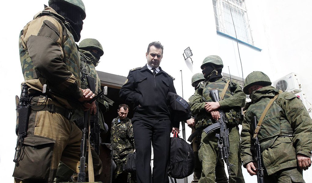 A Ukrainian naval officer (C) passes by armed men, believed to be Russian servicemen, as he leaves the naval headquarters in Sevastopol, March 19, 2014. Three Russian flags were flying at one of the entrances to Ukraine's naval headquarters in the Crimean