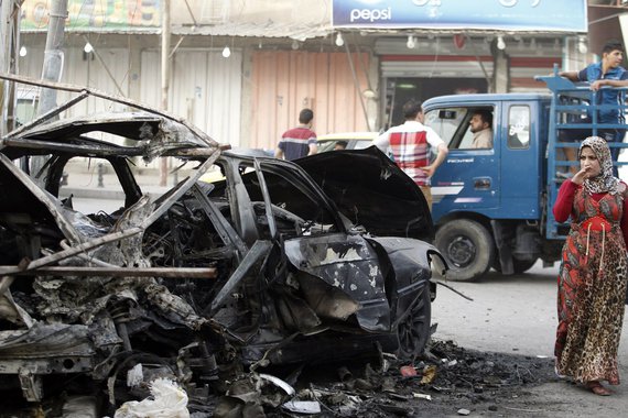 A woman looks at a destroyed vehicle as she walks past the site of a car bomb attack outside an ice cream parlour in the Al-Mashtal district of Baghdad, October 19, 2013. At least five people were killed in the attack and 15 others were wounded, police sa