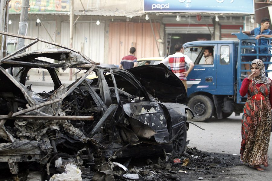 A woman looks at a destroyed vehicle as she walks past the site of a car bomb attack outside an ice cream parlour in the Al-Mashtal district of Baghdad, October 19, 2013. At least five people were killed in the attack and 15 others were wounded, police sa