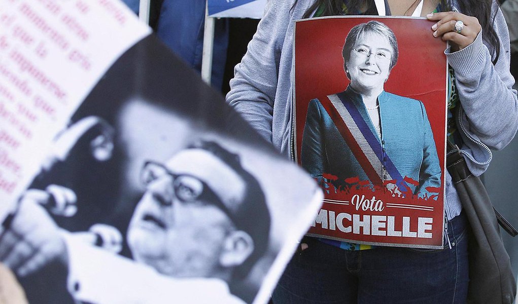 A supporter of Chilean presidential candidate Michelle Bachelet of Nueva Mayoria (New Majority) holds her poster next to a banner with an image of former Socialist president Salvador Allende, during a campaign event in Valparaiso city, about 121 km (75 mi