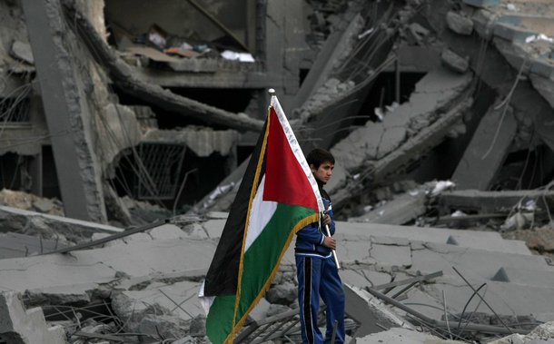 A Palestinian boy carries the national flag as he makes his way through the debris of the destroyed Palestine Sports Stadium in Gaza City on November 22, 2012, after a ceasefire took hold in and around Gaza after a week of cross-border violence between Is