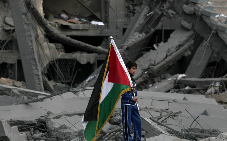 A Palestinian boy carries the national flag as he makes his way through the debris of the destroyed Palestine Sports Stadium in Gaza City on November 22, 2012, after a ceasefire took hold in and around Gaza after a week of cross-border violence between Is