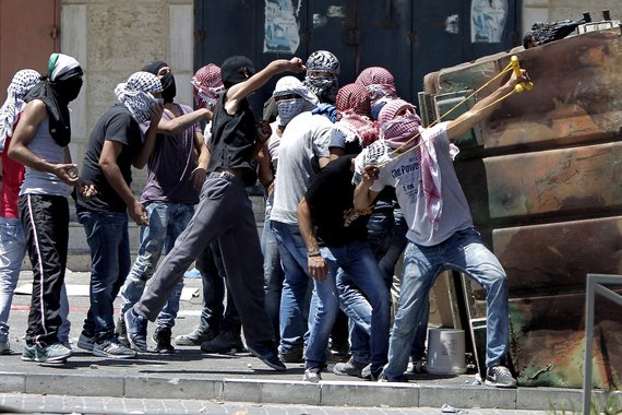 Palestinian protestors gather behind a barrier as they throw stones toward Israeli police during clashes in the Shuafat neighborhood in Israeli-annexed Arab East Jerusalem, on July 2, 2014, after a Palestinian teenager was kidnapped and killed in an appar