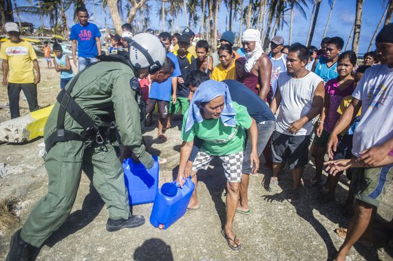 HENANE, Republic of the Philippines (Nov. 16, 2013) Naval Aircrewman (Tactical Helicopter) 2nd Class Jason Rimando, from Torrance, Calif., left, passes water containers to Filipino civilians in support of Operation Damayan. The George Washington Strike Gr