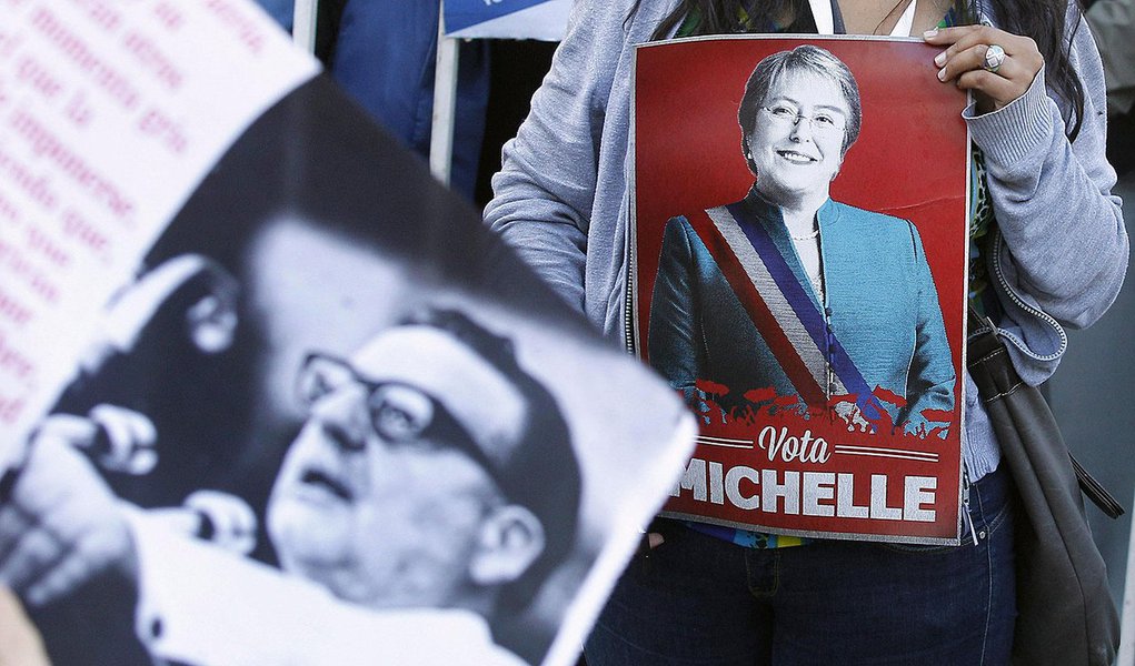 A supporter of Chilean presidential candidate Michelle Bachelet of Nueva Mayoria (New Majority) holds her poster next to a banner with an image of former Socialist president Salvador Allende, during a campaign event in Valparaiso city, about 121 km (75 mi