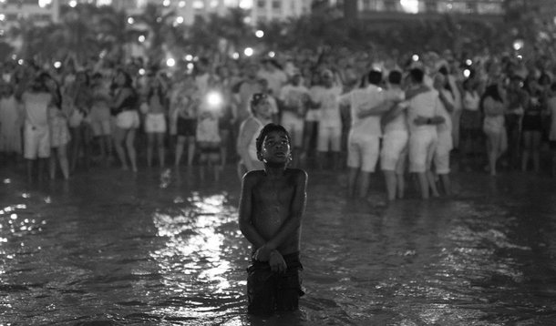 Imagem do fotógrafo Lucas Landau mostra um garoto negro e com frio dentro do mar, à frente de um grande grupo de pessoas vestidas de branco durante a queima de fogos do Ano Novo no Rio de Janeiro; postagem já teve mais de 20 mil reações e mais de 5 mil compartilhamentos; "A fotografia abre margem para várias interpretações; todas legítimas", comentou Landau, depois da repercussão