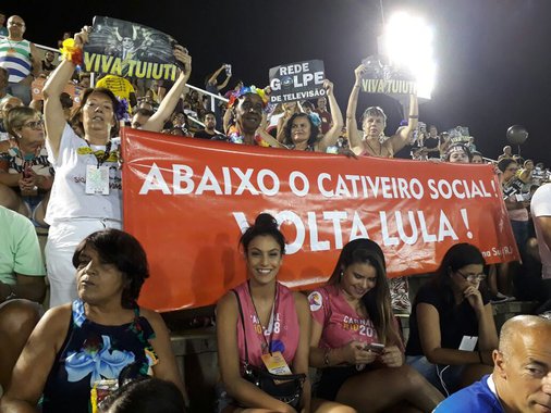 Algumas pessoas presentes na reapresentação do desfile seguravam uma faixa que dizia: "Abaixo o cativeiro social. Volta Lula!"; apesar de ser vítima de intensa caçada judicial e condenado sem provas, o petista segue líder absoluto em todas as pesquisas e já foi apontado como o melhor presidente da história, segundo levantamentos oficiais; enquanto isso, Michel Temer é rejeitado por mais de 90% dos brasileiros e coloca em prática uma dura política que implica em retrocessos sociais