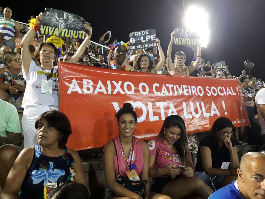 Algumas pessoas presentes na reapresentação do desfile seguravam uma faixa que dizia: "Abaixo o cativeiro social. Volta Lula!"; apesar de ser vítima de intensa caçada judicial e condenado sem provas, o petista segue líder absoluto em todas as pesquisas e já foi apontado como o melhor presidente da história, segundo levantamentos oficiais; enquanto isso, Michel Temer é rejeitado por mais de 90% dos brasileiros e coloca em prática uma dura política que implica em retrocessos sociais