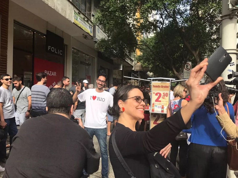 Chamado de 'esfihaço', um ato solidário reuniu centenas de cariocas em apoio ao refugiado sírio Mohammed Ali, vítima de xenofobia recentemente no Rio de Janeiro; o imigrante, que vende salgados árabes numa calçada em Copacabana, foi agredido verbalmente por um vendedor ambulante, que exigia que ele saísse do Brasil; a fila para comprar esfihas e quibes era formada por um número de 20 a 30 pessoas; Mohamed ficou o tempo todo ocupado, ora atendendo os pedidos, ora no caixa; ele só parava por poucos segundos para atender a pedidos de fotos dos clientes