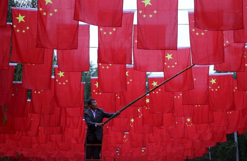 Homem colocando bandeiras chinesas em parque em Pequim. 29/09/2015 REUTERS/China Daily