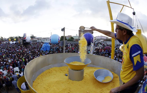 No São João de Caruaru, em Pernambuco, um dos dois maiores do país, a celebração da comida à base de milho, típica dos festejos de junho, é levada a sério pela população; neste domingo, o Festival de Comidas Gigantes da cidade teve seu ponto alto com a Caminhada do Forró e a distribuição do cuscuz que a organização promete ser "o maior do mundo", que foi distribuído às 17h; foram usados 800 quilos de floco de milho para produzir o alimento; a cuscuzeira, de 4,2 metros, feita sob medida na Feira de Caruaru, precisou de uma escada pra que os funcionários chegassem até a tampa; para abrir, foi montado um sistema de roldanas