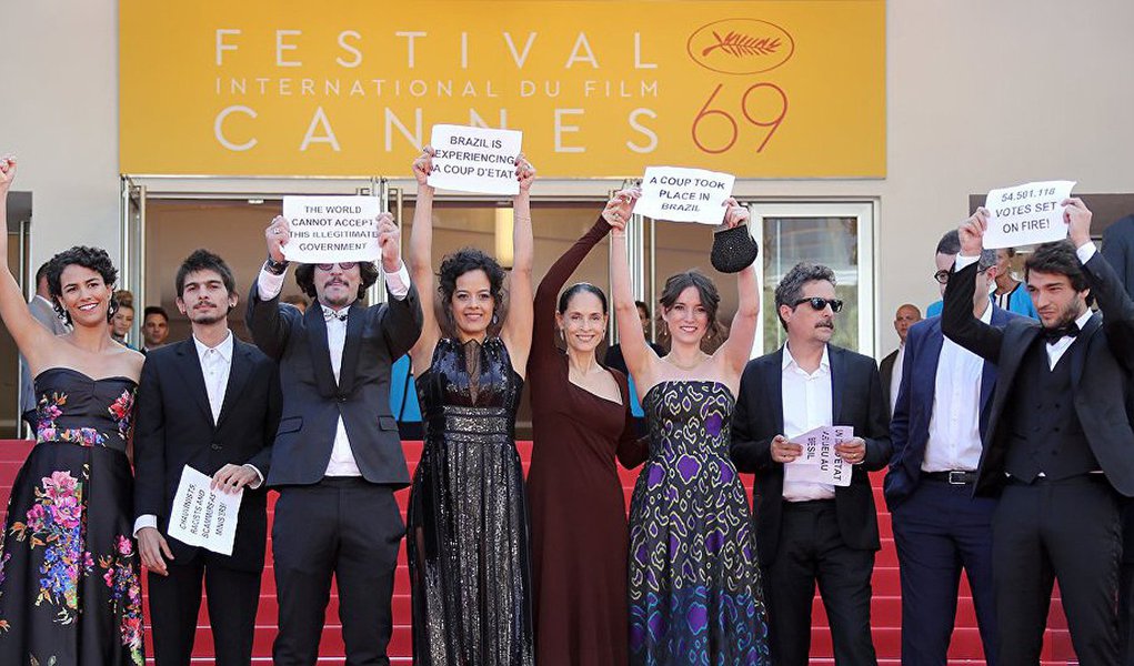 Ministério da Justiça determinou que o filme Aquarius, do cineasta Kleber Mendonça Filho, fosse classificado como impróprio para menores de 18 anos sob a alegação de que possui "situação sexual complexa"; elenco do filme, estrelado por Sônia Braga, fez um protesto contra o presidente interino, Michel Temer, durante o Festival de Cannes, na França; os atores exibiram cartazes condenando o golpe no Brasil e ganharam as capas de jornais no mundo