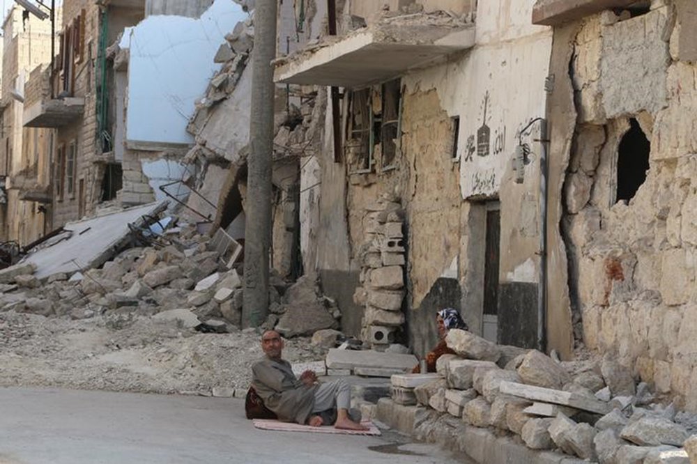 Residents rest on the ground near rubble in a damaged neighbourhood in Aleppo, Syria July 30, 2015. REUTERS/Abdalrhman Ismail