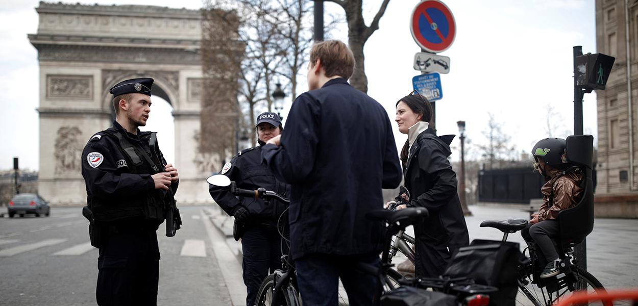 Policiais franceses conversam com ciclistas em frente ao Arco do Triunfo durante bloqueio pelo coronavírus
