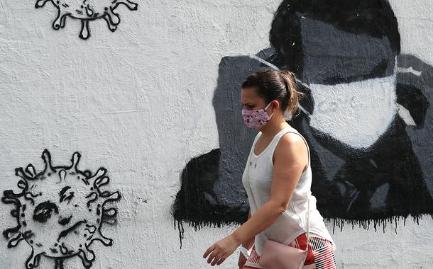 Mulher passa por grafite do presidente Jair Bolsonaro ajustando sua máscara protetora e em forma de vírus, em meio ao surto de Covid-19 no Rio de Janeiro.