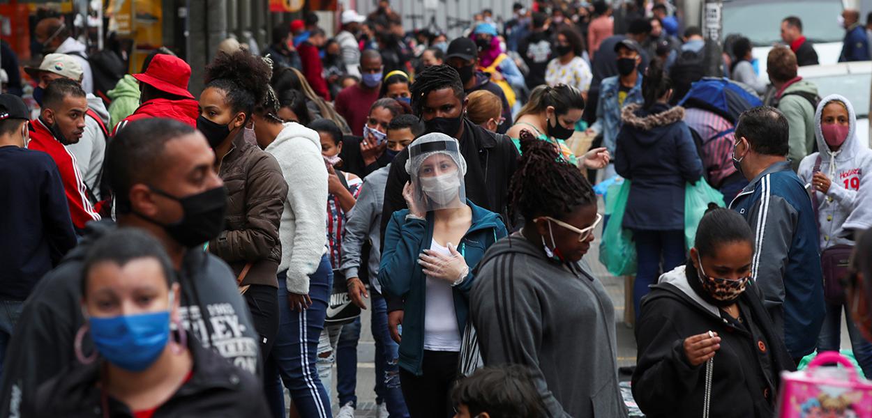 Pessoas com máscaras de proteção facial caminham em rua de comércio popular em São Paulo