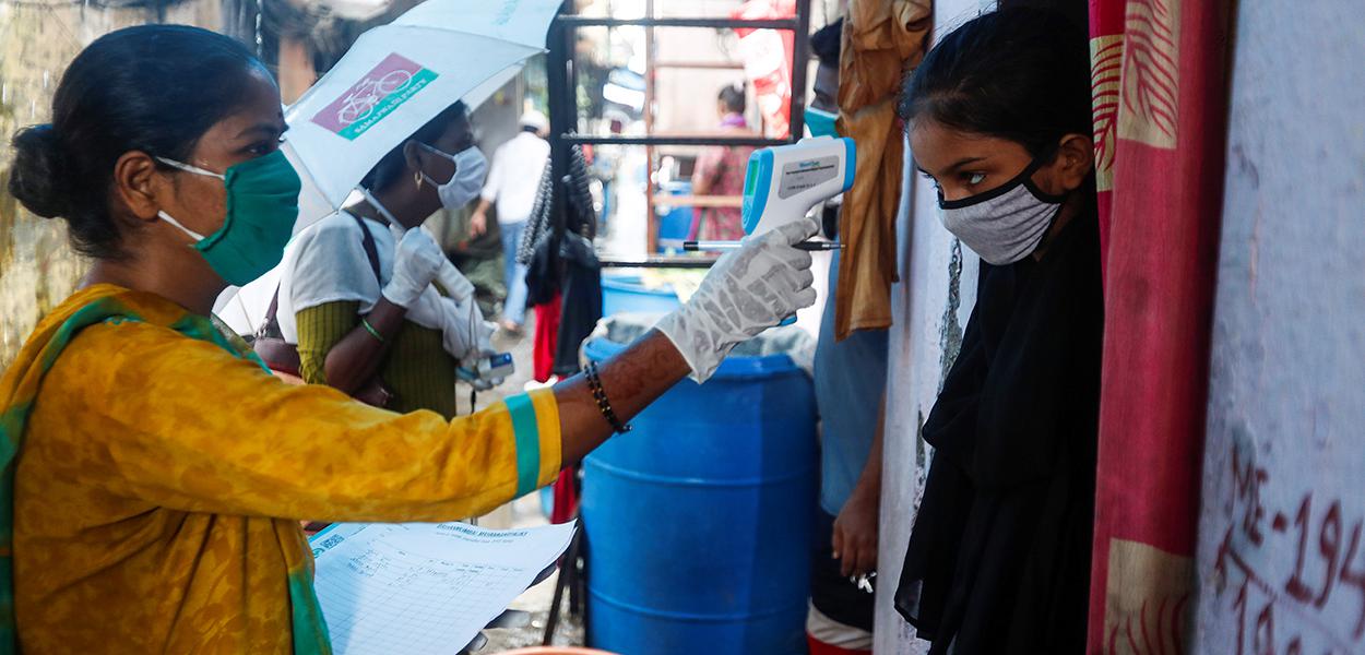 Voluntária que atua na medicina comunitária checa temperatura de garota em favela de Mumbai, na Índia