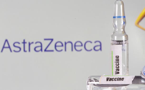 Tubo de ensaio com o rótulo de vacina em frente a logo da AstraZeneca em foto de ilustração