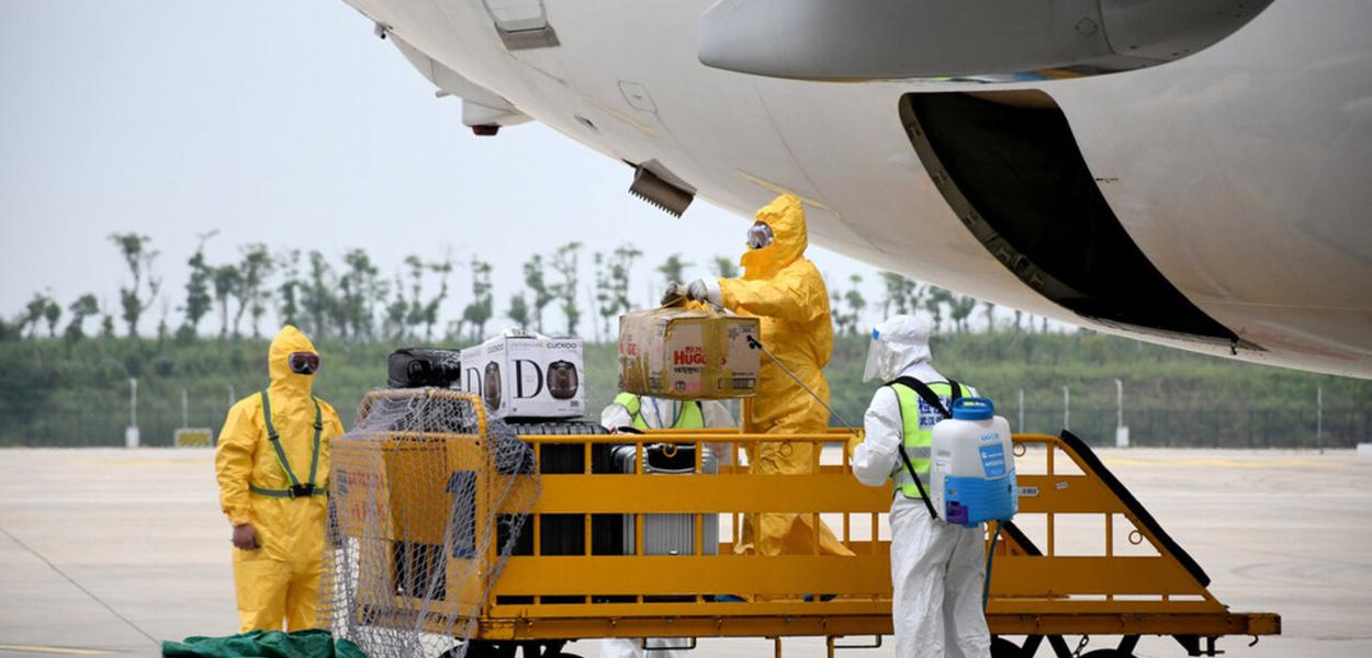 Trabalhadores em trajes de proteção desinfetam bagagens que chegam no Aeroporto Internacional de Wuhan