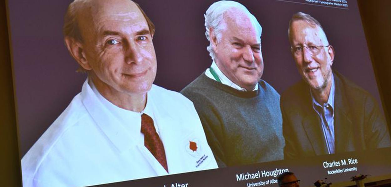 Fotos dos cientistas Harvey J. Alter, Michael Houghton e Charles M. Rice aparecem em tela durante anúncio de vencedores do Prêmio Nobel de Medicina em Estocolmo