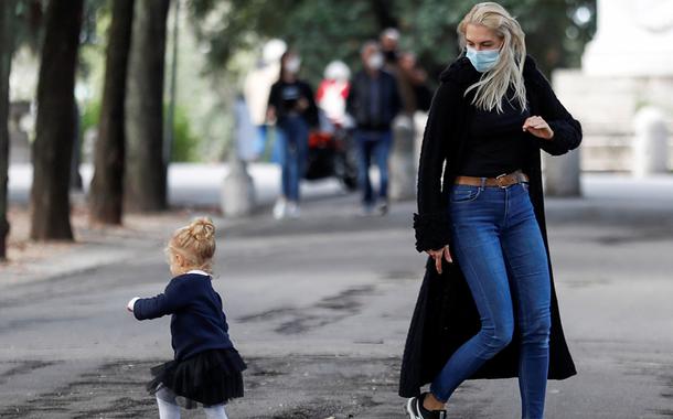 Mulher usando máscara brinca com criança em Roma