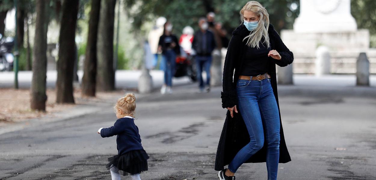 Mulher usando máscara brinca com criança em Roma