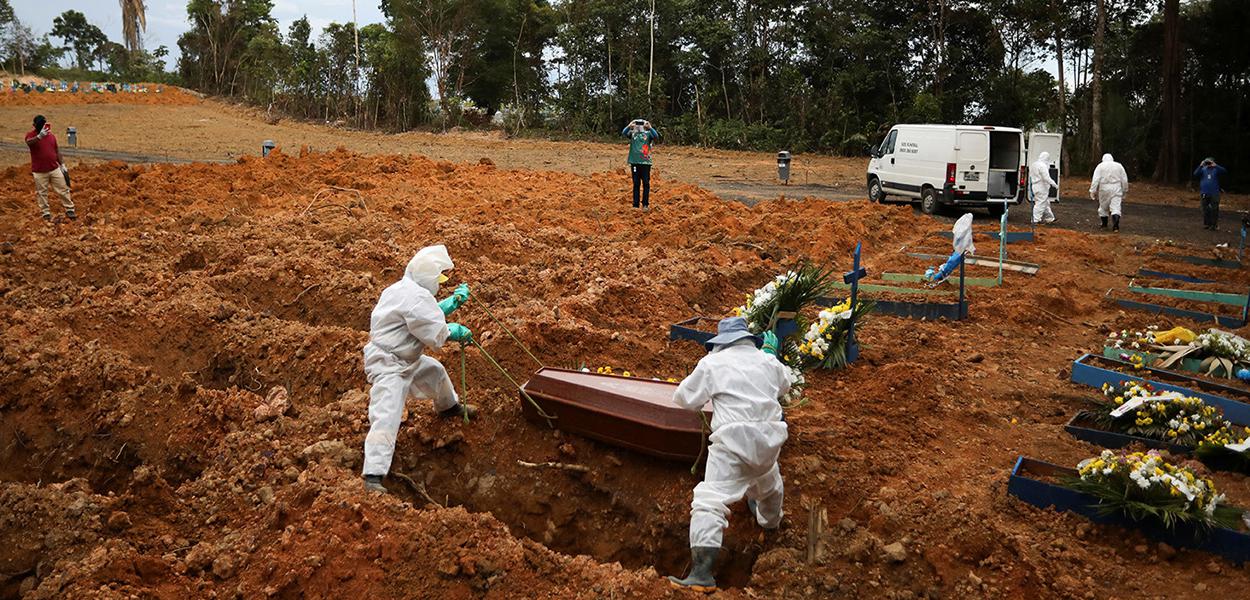 Coveiros vestindo roupas de proteção se preparam para enterrar no cemitério Parque Taruma, em Manaus.