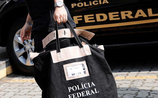 Agente carrega uma bolsa ao chegar à sede da Polícia Federal em São Paulo