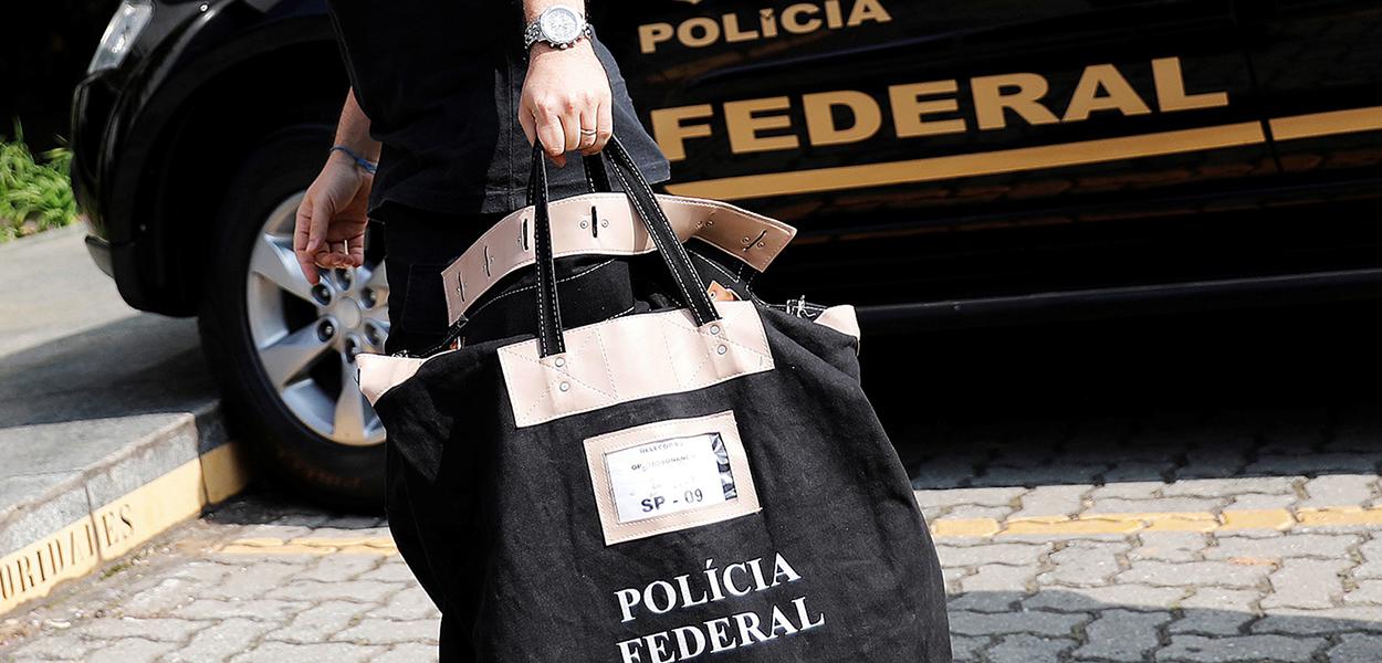 Agente carrega uma bolsa ao chegar à sede da Polícia Federal em São Paulo