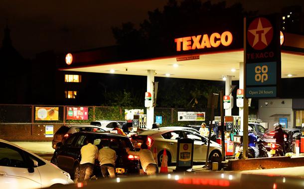 Pessoas empurram carro em fila de veículos diante de posto de combustível no sul de Londres26/09/2021