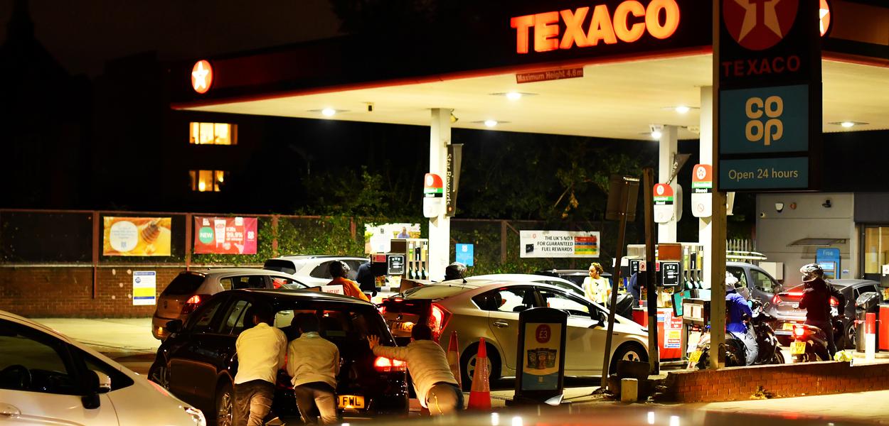 Pessoas empurram carro em fila de veículos diante de posto de combustível no sul de Londres26/09/2021
