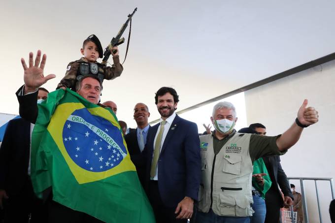 Bolsonaro se enrola na bandeira nacional para foto com criança segurando arma de brinquedo