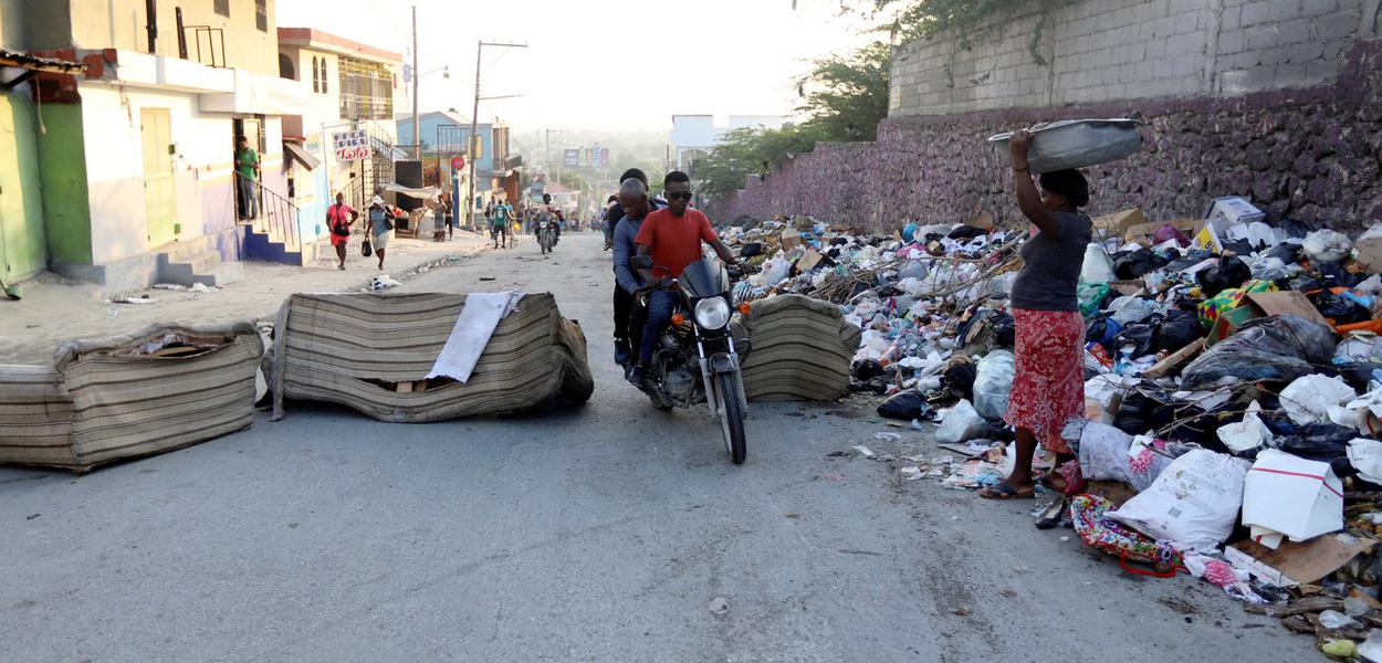 Pessoas passam por barricada em rua de Porto Príncipe, no Haiti