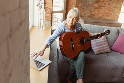 Learning to play guitar online. Senior woman studying at home, getting online courses, self-development. Caucasian woman using modern devices for education, spending time for new job or hobby.