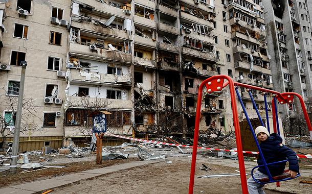 Criança em balanço em frente a prédio residencial danificado em Kiev após Rússia lançar ataque maciço à capital ucraniana 25/02/2022