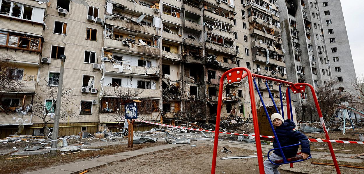 Criança em balanço em frente a prédio residencial danificado em Kiev após Rússia lançar ataque maciço à capital ucraniana 25/02/2022