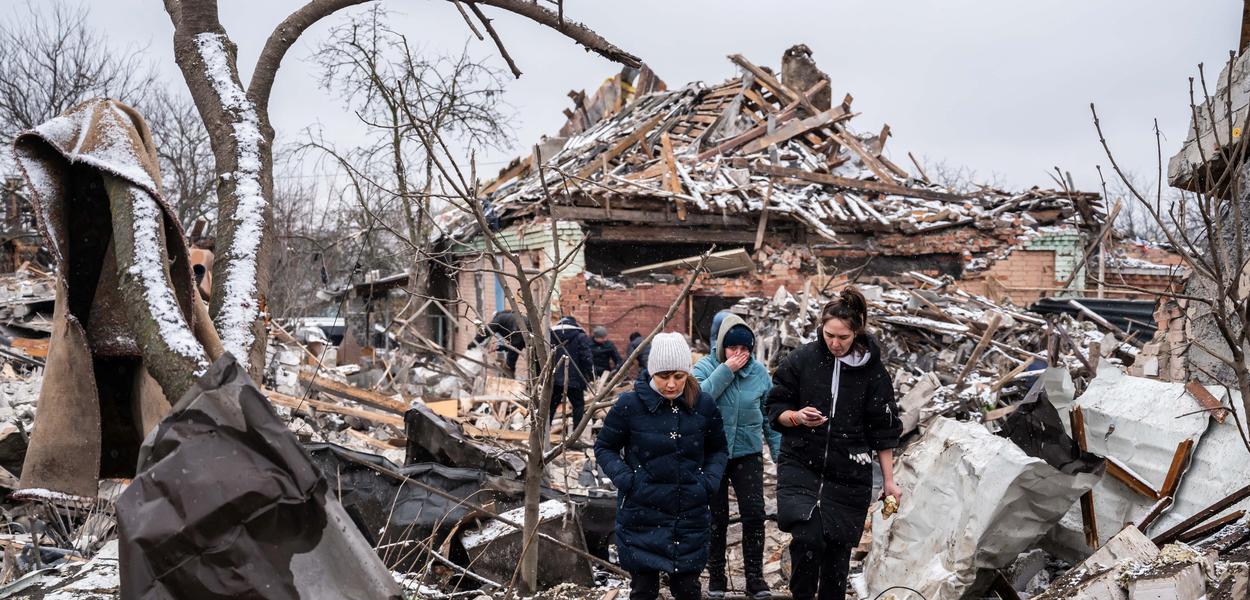 Mulheres caminham em meio a destroços de prédios residenciais destruídos por bombardeio