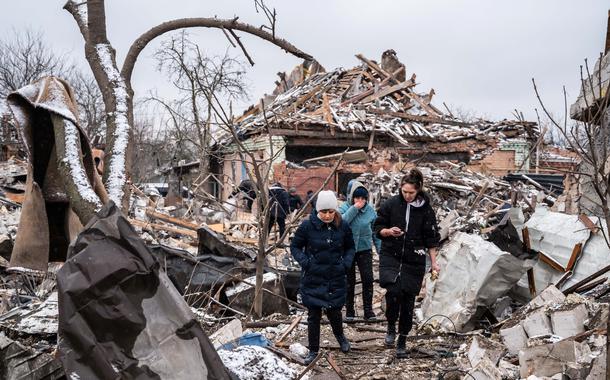 Mulheres caminham em meio a destroços de prédios residenciais destruídos por bombardeio