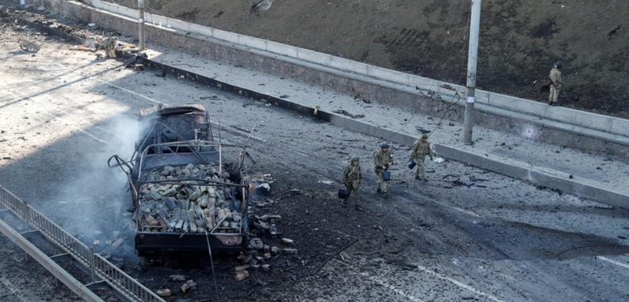 Militares ucranianos passam por um veículo danificado, no local de um combate com tropas russas em Kiev, Ucrânia, em 26 de fevereiro